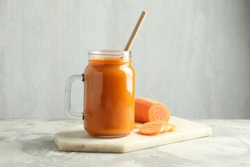 Fresh carrot juice in mason jar and vegetable on gray textured table