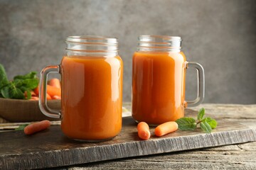 Fresh carrot juice in mason jars, vegetables and mint on wooden table against gray background