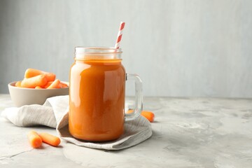 Fresh carrot juice in mason jar and vegetables on gray textured table, space for text