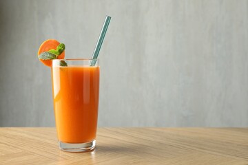 Fresh carrot juice in glass on wooden table against gray background, space for text