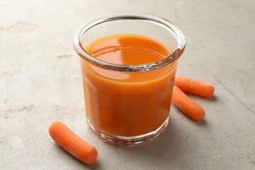 Fresh carrot juice in glass and vegetables on gray textured table