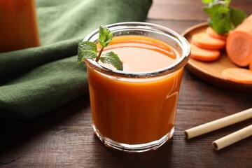 Fresh carrot juice in glass, vegetables, mint and straws on wooden table