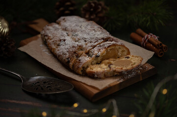 Slices of German Christmas stollen cake on a wooden cutting board on rustic background with lights and decorations. Traditional handmade Christmas dessert. Fruit bread with nuts, raisins and marzipan.