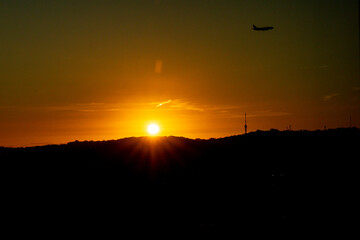 Lisbon, Portugal - Silhouette of a commercial airplane landing at sunset  with the hills of the Parque Florestal de Monsanto in the foreground