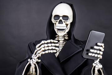 Skeleton in hoodie holding cell phone. Skeleton on gray background of smartphone. Mannequin cloak a smartphone skeleton. A mannequin cloak with a gray skeleton on a smartphone background lifestyle.