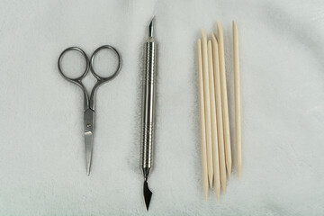 Manicure scissors, pusher, and orange cuticle sticks placed on a towel, depicting a manicure...