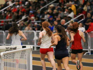 Women Compete in Track Race During Indoor Athletic Event With Crowd in Attendance