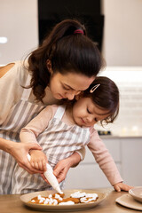 happy mother and little child girl bake cookies on the kitchen at home