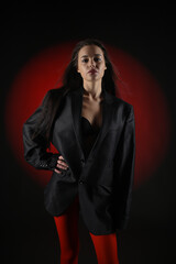 Beautiful girl in a black oversized blazer and red tights posing on a dark background.