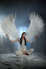 Beautiful angel woman in white clothing with large white wings posing on a white background..