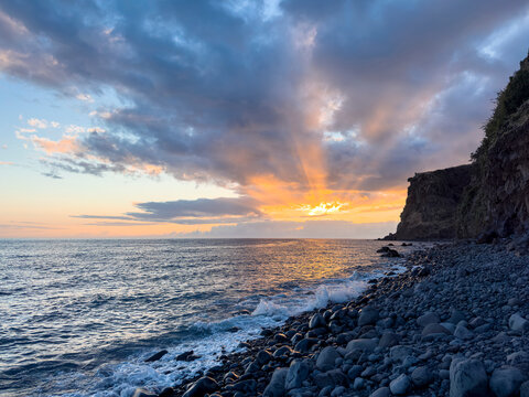 Sunset on a rocky ocean shore in Madeira, Portugal.
 - Powered by Adobe