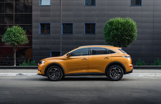 Orange SUV on the street in downtown district. Side profile view of french crossover DS7 Crossback parked in a city near modern building. Kyiv, Ukraine - June 11 2020.	