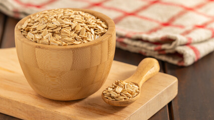 Wooden bowl and spoon filled with rolled oats on a cutting board, with a rustic cloth in the background. Ideal for healthy food and organic themes.