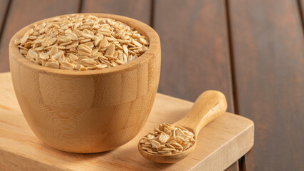 Wooden bowl and spoon filled with rolled oats on a cutting board, set against a rustic wooden background. Ideal for themes of healthy eating and organic food