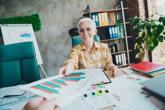 Photo of senior woman take papers graph secretary wear yellow print shirt formalwear comfy modern office room interior indoors workspace