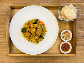 Chicken rendang with authentic Indonesian herbs and seasoned rice. Served with prawn crackers, marinated cucumber, and chili sauce dressing, on a wooden tray, on a wood rustic table.