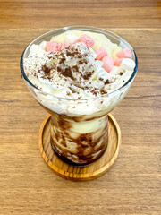 Avocado coffee sundae mixed with choco powder and vanilla ice cream with colorful marshmallow. A refreshing avocado frappe dessert served on a dessert glass on a wooden rustic table.