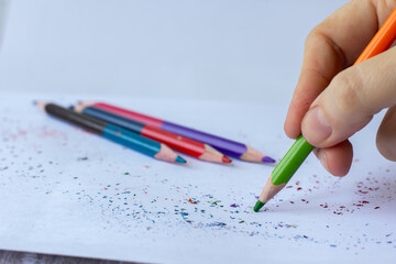female hand writing with colored pencil on white sheet of paper
