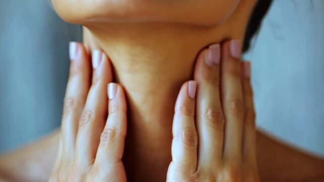 A person touching their neck in discomfort, indicating symptoms of a swollen thyroid gland.