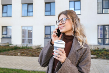 A young woman holding a smartphone in one hand and a cup of coffee in the other, combining comfort with technology and multitasking in her daily life.