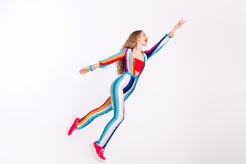 Young woman in a colorful striped jumpsuit with long blond hair happily poses against a white...