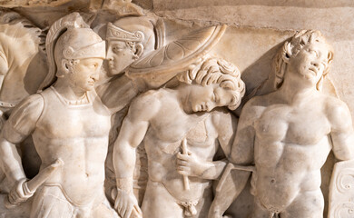 Close-up on sculptures carved in a marble wall representing naked ancient greek soldiers