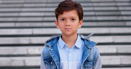 Young boy, portrait and freckles with fashion on staircase for school, childhood or stylish clothing in city. Child, teenager or face of casual kid with denim jacket, shirt or stairs in an urban town