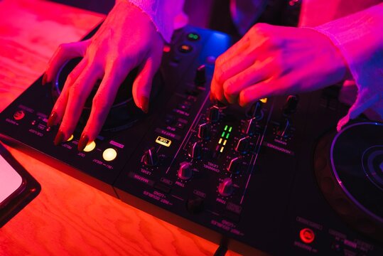 Close-up of a person&rsquo;s hands with red painted nails adjusting knobs and sliders on a DJ controller