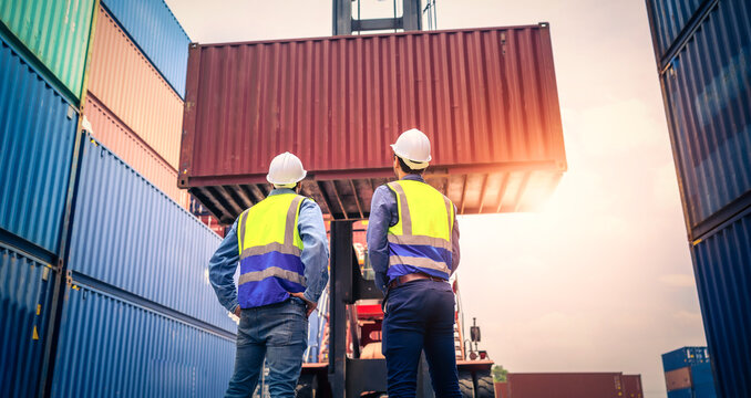 Two Engineer or foreman wears PPE checking container storage with cargo container background at sunset. Logistics global import or export shipping industrial concept.