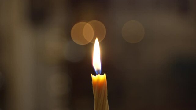 A single white candle burning. Yellow paraffin candle with yellow shades burns on a black background. Slow motion.