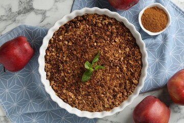 Tasty apple crisp in baking dish, fresh fruits and cinnamon on white marble table, flat lay