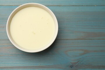 Condensed milk in bowl on light blue wooden table, top view. Space for text