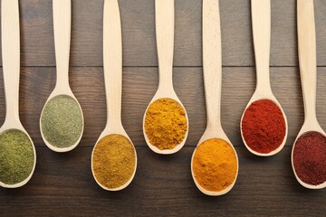 Different aromatic spices in spoons on wooden table, flat lay