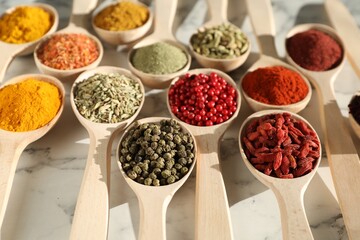 Different aromatic spices in spoons on white marble table, closeup