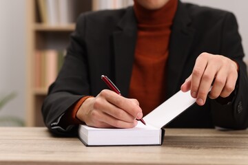 Writer signing autograph in book at wooden table indoors, closeup