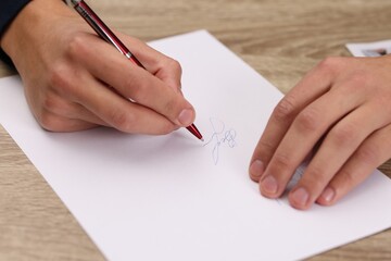 Writer signing autograph on sheet of paper at wooden table, closeup