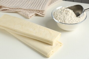 Raw puff pastry dough and flour on white table