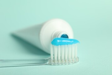 Toothbrush with toothpaste and tube on light blue background, closeup