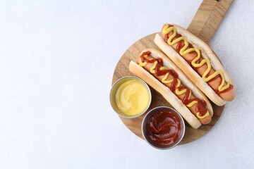 Tasty hot dogs with ketchup and mustard on light table, top view. Space for text