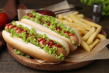 Tasty hot dogs with lettuce, ketchup and potato fries on wooden table, closeup