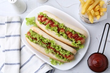 Tasty hot dogs with lettuce, ketchup and potato fries on white table, flat lay