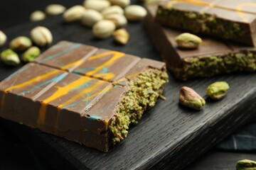 Pieces of Dubai chocolate bars with pistachios and knafeh on black table, closeup