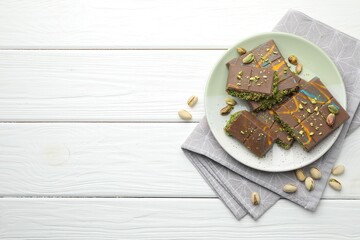 Pieces of Dubai chocolate bars with pistachios and knafeh on white wooden table, flat lay. Space for text