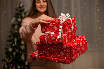 Smiling Woman Holding Christmas Gift in Light Pink Sweater by Decorated Tree, Cozy Holiday Scene with Twinkling Lights, Warm Winter Atmosphere, Festive Spirit, Joyful Christmas and New Year