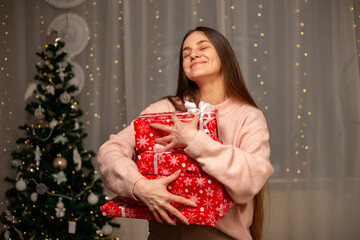 Smiling Woman Holding Christmas Gift in Light Pink Sweater by Decorated Tree, Cozy Holiday Scene with Twinkling Lights, Warm Winter Atmosphere, Festive Spirit, Joyful Christmas and New Year