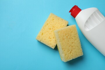 Sponges and dish soap on light blue background, top view. Space for text