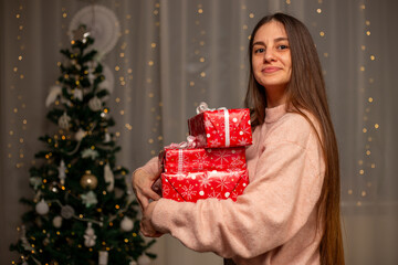 Smiling Woman Holding Christmas Gift in Light Pink Sweater by Decorated Tree, Cozy Holiday Scene with Twinkling Lights, Warm Winter Atmosphere, Festive Spirit, Joyful Christmas and New Year