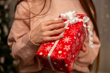 Smiling Woman Holding Christmas Gift in Light Pink Sweater by Decorated Tree, Cozy Holiday Scene with Twinkling Lights, Warm Winter Atmosphere, Festive Spirit, Joyful Christmas and New Year