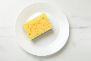 Yellow sponge and plate on white table, top view