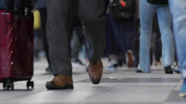 Shoes and feet of people walking in a crowded Tokyo subway train station during rush hour circa 2024.